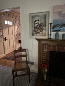 Photograph of the Flowers on a Chair painting on display with the chair that it reperesents on the floor in front of it.